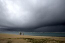 FILE - People hold umbrellas as it begins to rain on an otherwise empty beach in Honolulu on Monday, Dec. 6, 2021.