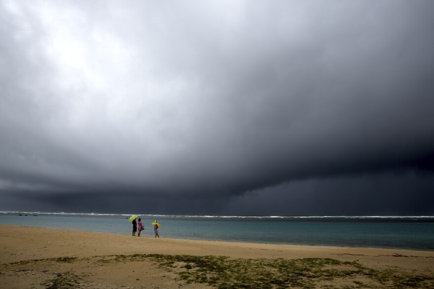 FILE - In this Aug. 24, 2018 file photo, a man and his son watch as waves crash off sea cliffs along the southeast shore of Oʻahu as Hurricane Lane approaches Honolulu. (AP Photo/Caleb Jones, File)