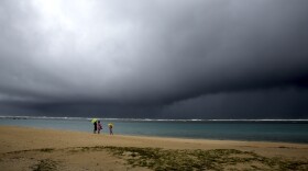 FILE - People hold umbrellas as it begins to rain on an otherwise empty beach in Honolulu on Monday, Dec. 6, 2021.