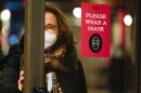 FILE - A woman walks through a door with a sign asking shoppers to wear masks, in New York, Feb. 9, 2022.