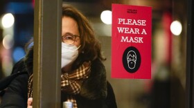 FILE - A woman walks through a door with a sign asking shoppers to wear masks, in New York, Feb. 9, 2022.