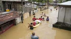 Residents give out free food as they wade through a flooded street in their village from Typhoon Noru in San Miguel town, Bulacan province, Philippines, Monday, Sept. 26, 2022. Typhoon Noru blew out of the northern Philippines on Monday, leaving some people dead, causing floods and power outages and forcing officials to suspend classes and government work in the capital and outlying provinces. (AP Photo/Aaron Favila)