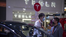 Staff members talk near vehicles at a display for automaker Tesla at the China International Fair for Trade in Services (CIFTIS) in Beijing, Friday, Sept. 2, 2022. (AP Photo/Mark Schiefelbein)