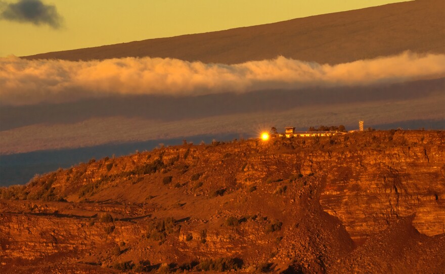 Sunrise illuminates the windows of the facilities on the bluff at Uēkahuna at the summit of Kīlauea. Maunaloa volcano looms above. (Jan. 25, 2024)