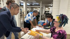 Democratic Party of Hawaiʻi interim chair Adrian Tam places his presidential caucus ballot for counting in an envelope held by party volunteer Bonnie Fraser in Honolulu on Wednesday, March 6, 2024.