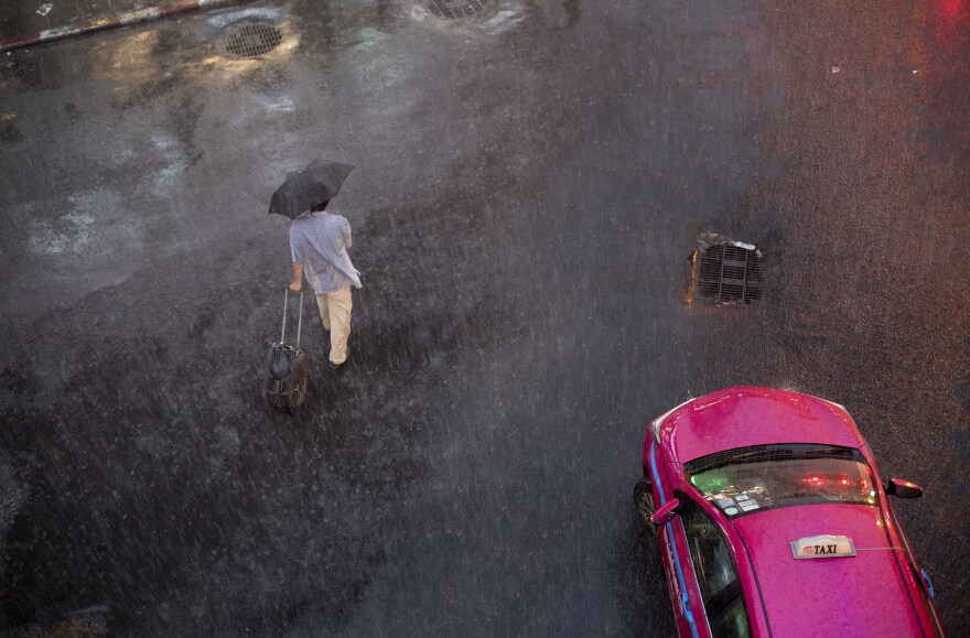 FILE - A man braves through rain on a road during a downpour in Bangkok, Thailand, Thursday, Aug 22, 2019. (AP Photo/Gemunu Amarasinghe)