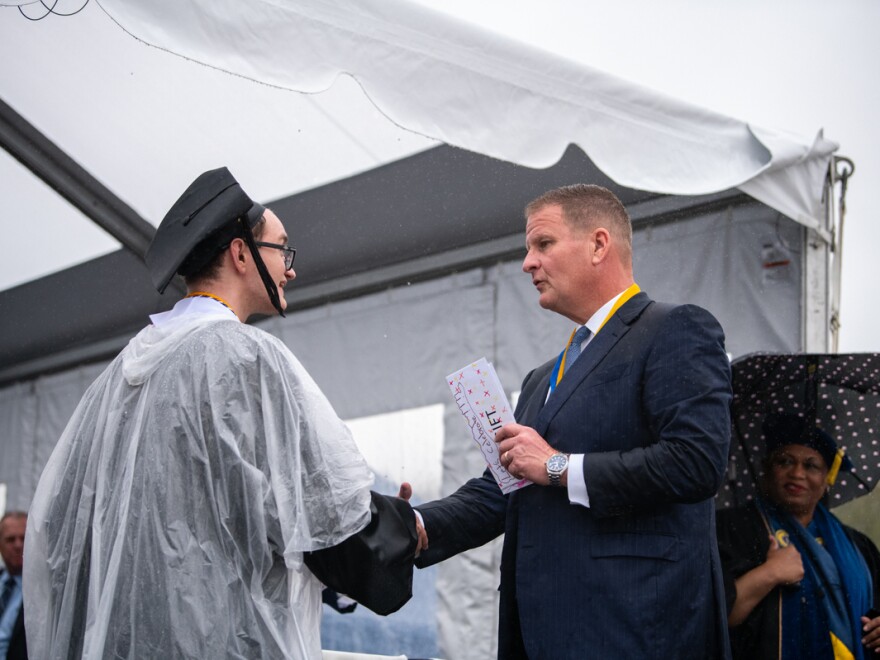 Robert Hale (right) gives an envelope with cash to a graduating UMass Dartmouth student at last week's commencement. Each of the 1,200 graduates received $1,000 onstage, half to keep and half to donate.