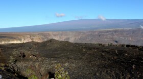 FILE - In this April 25, 2019 photo, Mauna Loa volcano, background, towers over the summit crater of Kīlauea volcano in Hawaiʻi Volcanoes National Park on the Big Island. (AP Photo/Caleb Jones)