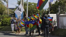 People demonstrate as French President Emmanuel Macron's motorcade drives past in in Noumea, New Caledonia, Thursday, May 23, 2024. Macron has landed in riot-hit New Caledonia, having crossed the globe by plane from Paris in a high-profile show of support for the French Pacific archipelago wracked by deadly unrest and where indigenous people have long sought independence from France. (Ludovic Marin/Pool Photo via AP)