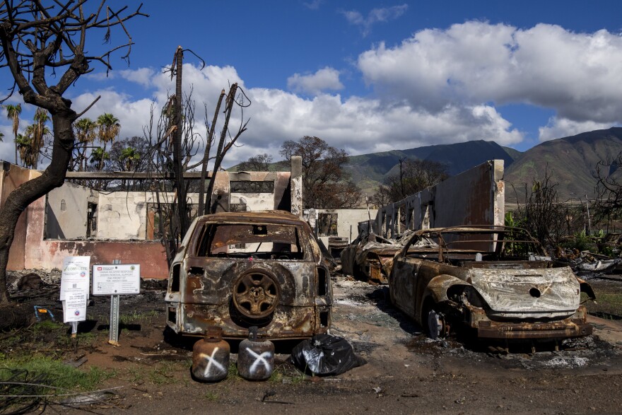 Burned cars and propane tanks with markings on them sit outside a house destroyed by wildfire, Friday, Dec. 8, 2023, in Lahaina, Hawaiʻi. (AP Photo/Lindsey Wasson)