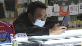 File - A smartphone seller wearing a face mask as a precaution against coronavirus outbreak waits for customers at a stall of a shopping mall in Jakarta, Indonesia, Monday, Jan. 4, 2021.