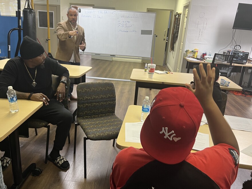 Freddy Barton (rear) and another adult mentor (left) counsel teen boys who've been arrested on gun crimes as part of the Tampa-based Youth Gun Offender program. During an evening session on Feb. 22, 2024, the group discussed a proposed state law to toughen penalties for kids who carry guns. The boy raising his hand argued spending time in juvenile jail can make kids more violent.