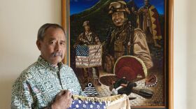 Vietnam Veteran Allen Hoe holds a battle flag and stands in front of a painting honoring his son Nainoa, who died in combat in the Iraq War.